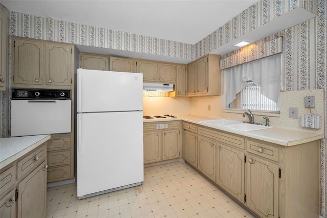 kitchen with under cabinet range hood, white appliances, a sink, light floors, and wallpapered walls