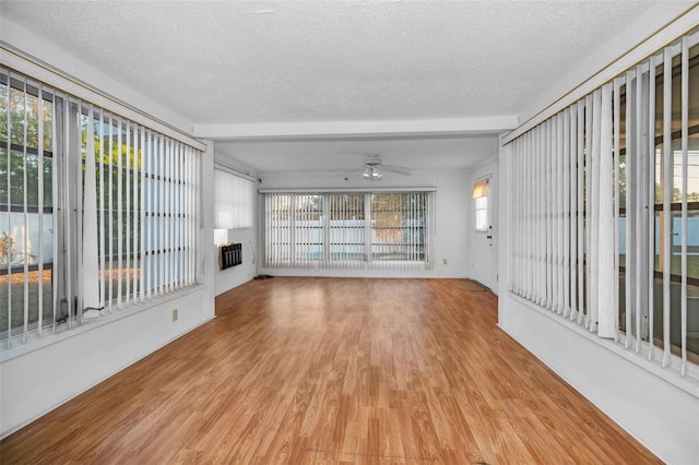 unfurnished living room with a textured ceiling, ceiling fan, plenty of natural light, and wood finished floors