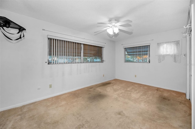 carpeted empty room with a textured ceiling, baseboards, and a ceiling fan