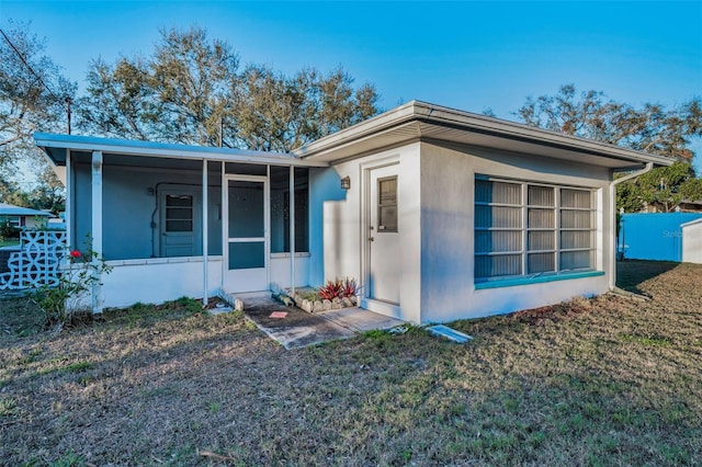 view of front of house with a sunroom, a front lawn, and stucco siding