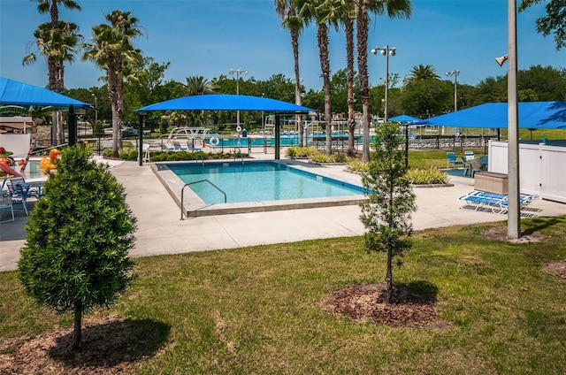 community pool with a lawn, a patio area, and fence