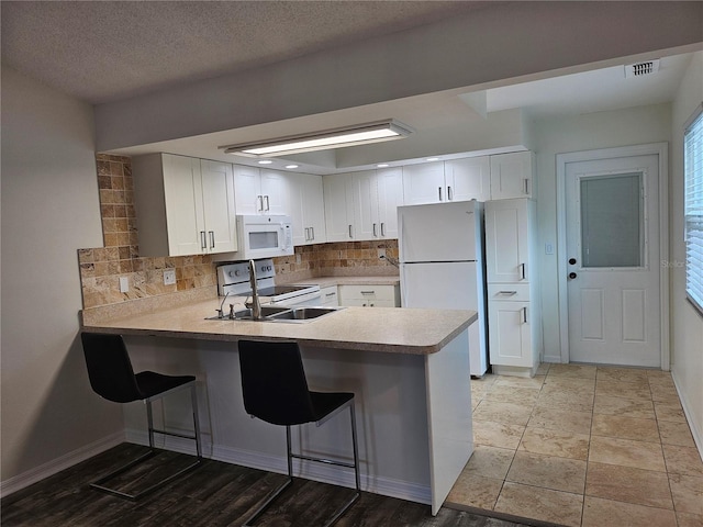 kitchen featuring a peninsula, white appliances, a kitchen breakfast bar, white cabinets, and decorative backsplash