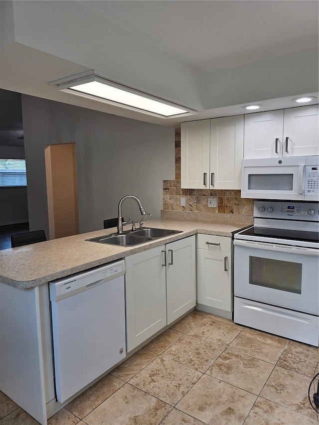 kitchen featuring a peninsula, white appliances, a sink, white cabinets, and tasteful backsplash