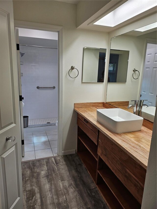 full bathroom featuring a skylight, a tile shower, wood finished floors, and vanity