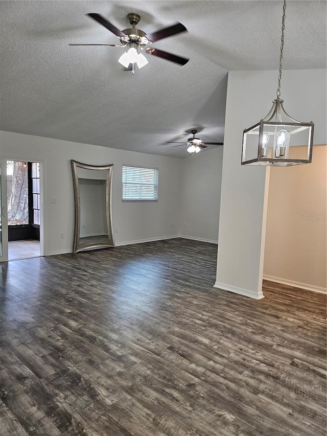 unfurnished living room with plenty of natural light, baseboards, dark wood finished floors, and ceiling fan with notable chandelier