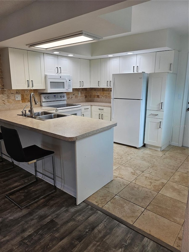 kitchen with a peninsula, white appliances, decorative backsplash, and white cabinets