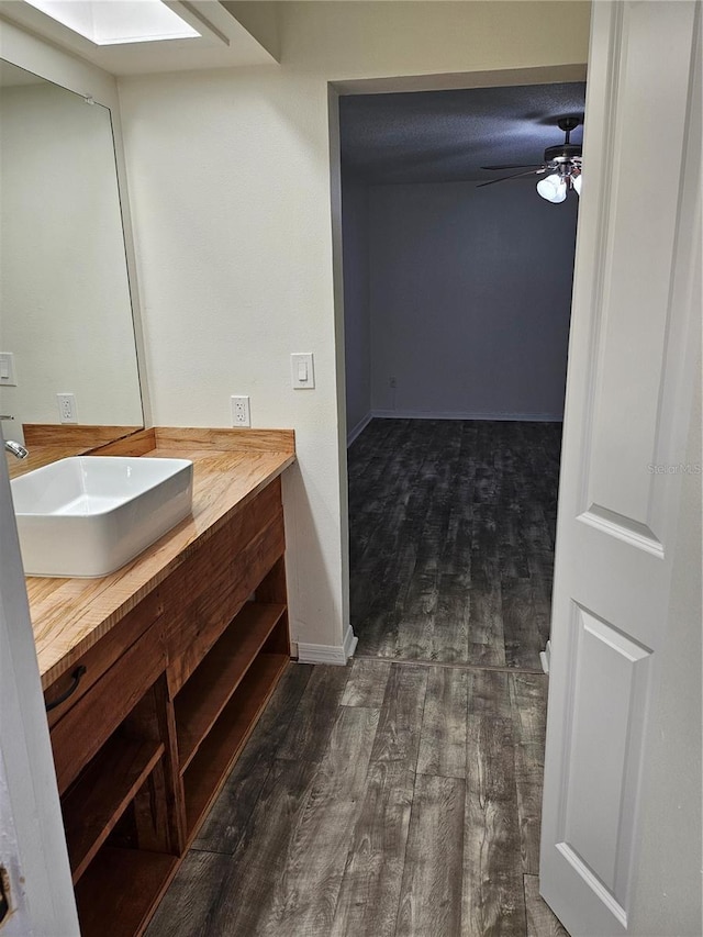 bathroom featuring a skylight, baseboards, a ceiling fan, wood finished floors, and vanity