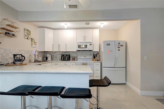 kitchen featuring backsplash, a sink, white appliances, a peninsula, and a kitchen bar