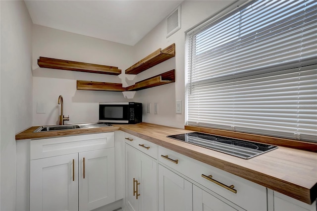 kitchen with open shelves, visible vents, white cabinetry, a sink, and butcher block countertops