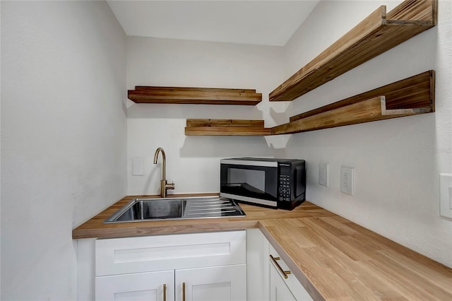 kitchen with black microwave, wood counters, white cabinetry, open shelves, and a sink