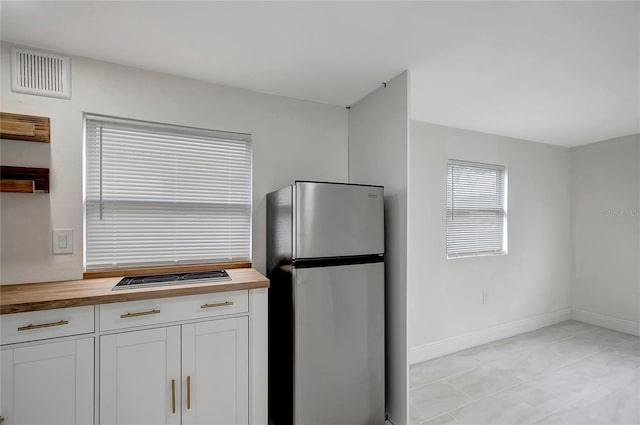 kitchen with visible vents, wooden counters, freestanding refrigerator, white cabinets, and baseboards