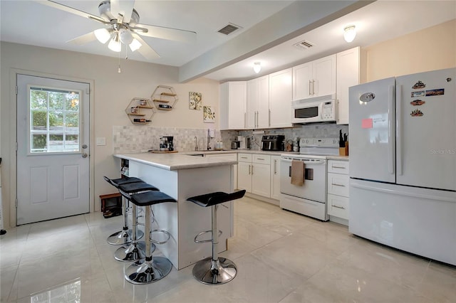 kitchen with a breakfast bar area, white appliances, white cabinetry, visible vents, and tasteful backsplash