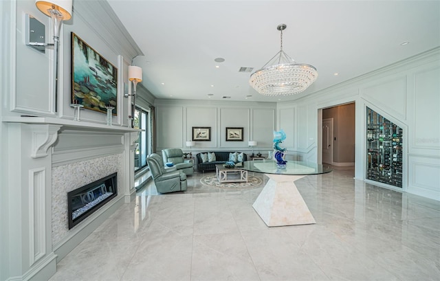 living area featuring crown molding, a glass covered fireplace, visible vents, and a decorative wall