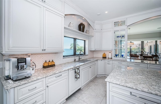 kitchen featuring light tile patterned floors, light stone counters, a sink, decorative backsplash, and crown molding