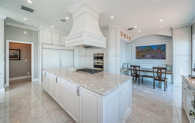 kitchen featuring visible vents, a kitchen island, custom exhaust hood, crown molding, and white cabinetry