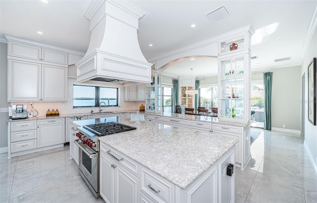 kitchen featuring stainless steel range, visible vents, ornamental molding, a sink, and premium range hood