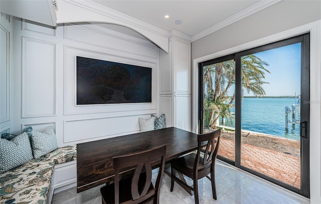 dining space featuring a water view, ornamental molding, a decorative wall, and light tile patterned flooring