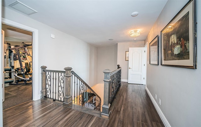 hall featuring baseboards, visible vents, wood finished floors, and an upstairs landing