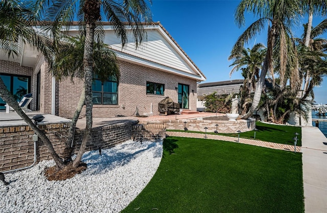 rear view of house featuring brick siding, a lawn, and a patio