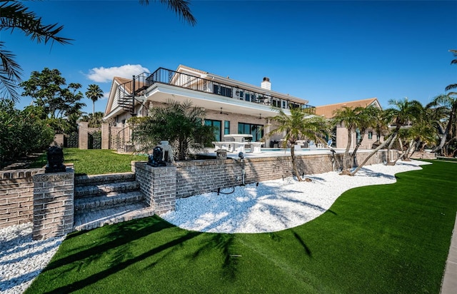 rear view of property with a balcony, a patio area, an outdoor pool, and a yard