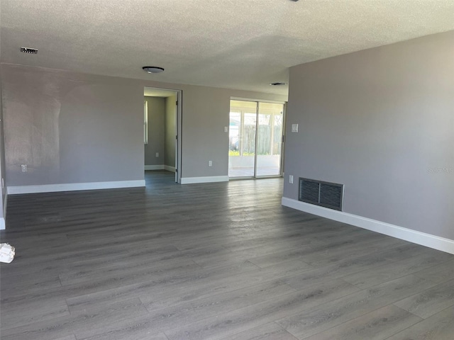 empty room with dark wood-style floors, baseboards, visible vents, and a textured ceiling