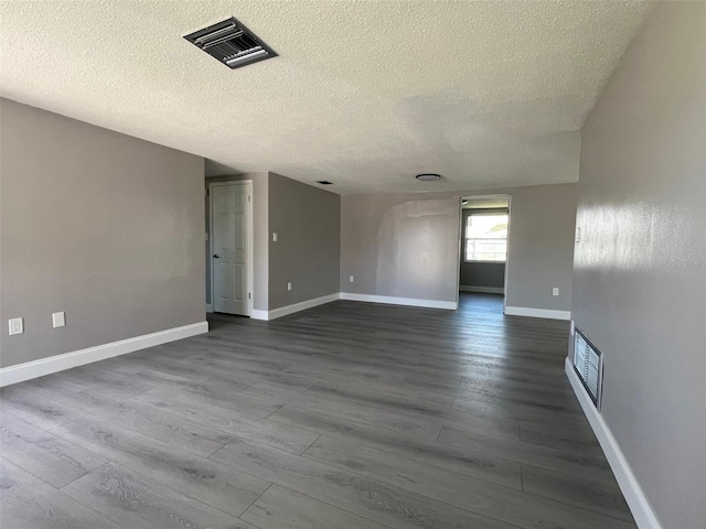 unfurnished room featuring baseboards, visible vents, dark wood finished floors, and a textured ceiling