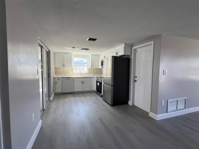 kitchen featuring wood finished floors, a sink, visible vents, appliances with stainless steel finishes, and tasteful backsplash