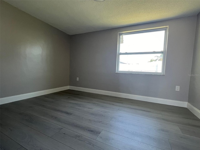 empty room with a textured ceiling, dark wood-type flooring, and baseboards