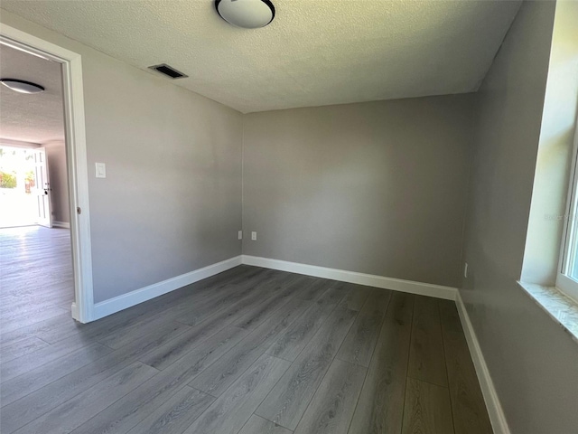 empty room featuring baseboards, a textured ceiling, visible vents, and dark wood-style flooring