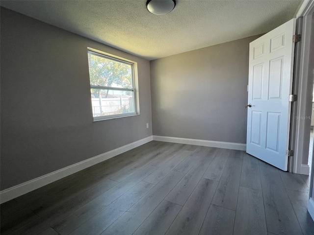 spare room with dark wood-style flooring, a textured ceiling, and baseboards