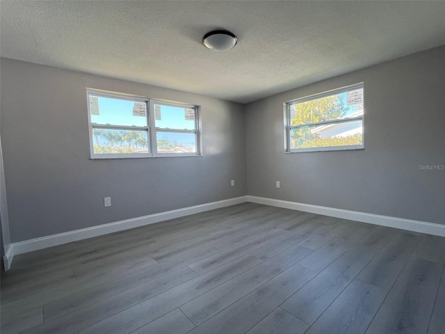 spare room with plenty of natural light, a textured ceiling, baseboards, and dark wood-type flooring