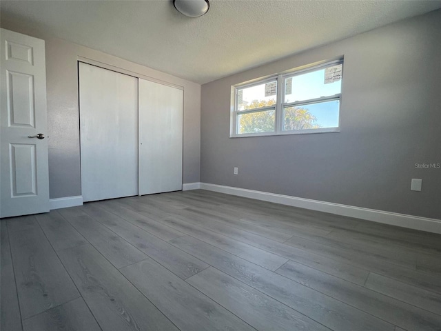 unfurnished bedroom featuring a textured ceiling, a closet, baseboards, and wood finished floors