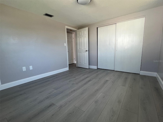 unfurnished bedroom featuring baseboards, a closet, visible vents, and wood finished floors