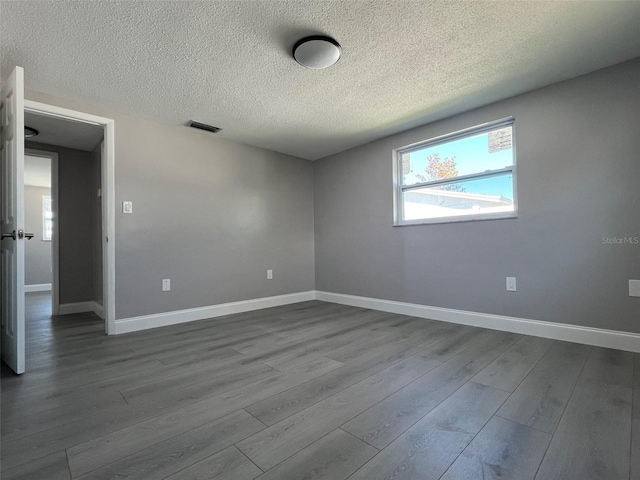 empty room with dark wood-style floors, a textured ceiling, and baseboards