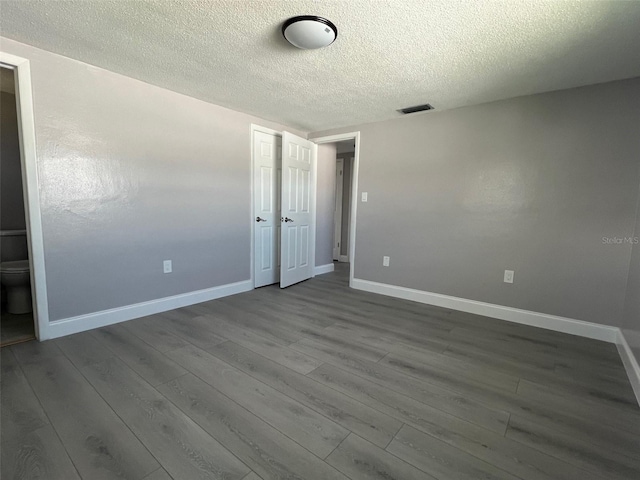 unfurnished room with a textured ceiling, dark wood finished floors, visible vents, and baseboards