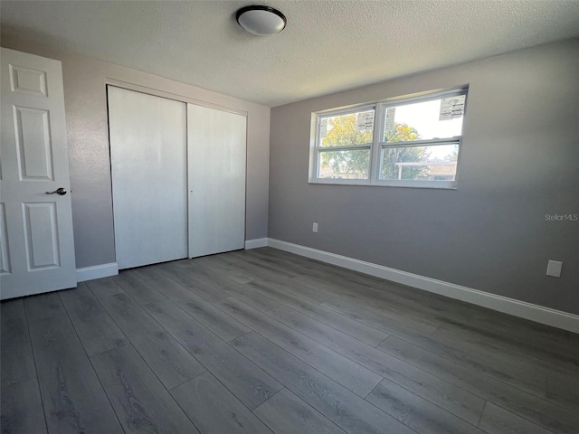 unfurnished bedroom with a closet, dark wood finished floors, a textured ceiling, and baseboards