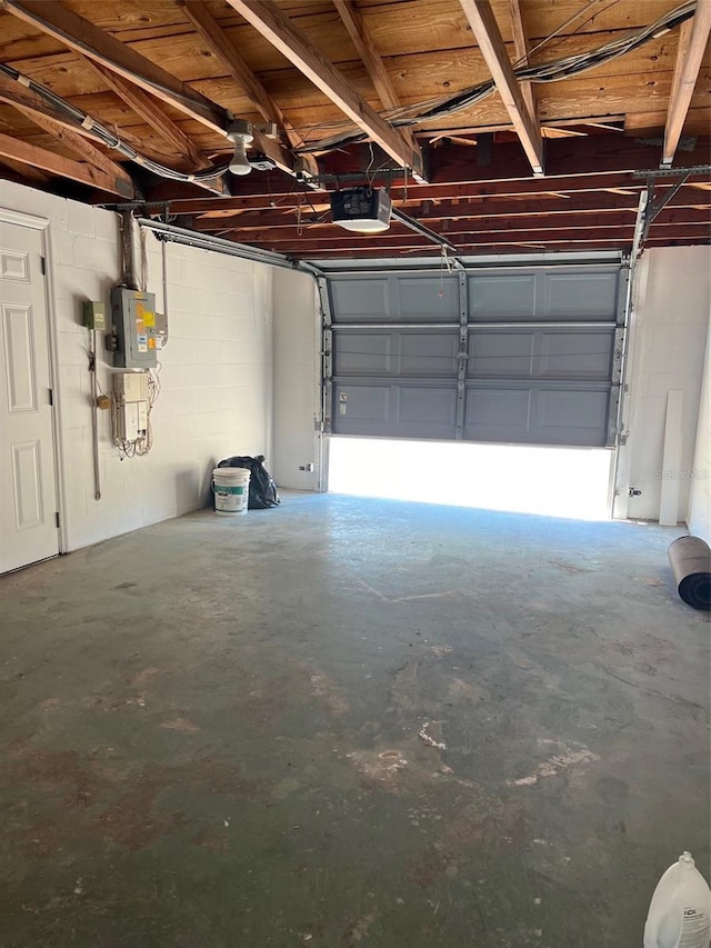 garage featuring concrete block wall, electric panel, and a garage door opener