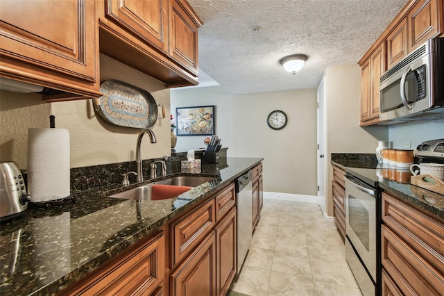 kitchen with stainless steel appliances, brown cabinetry, a sink, and dark stone countertops