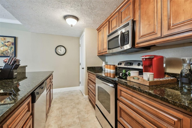 kitchen featuring stainless steel appliances, dark stone counters, brown cabinetry, and a textured ceiling