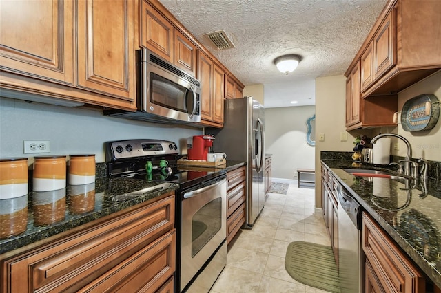 kitchen featuring visible vents, appliances with stainless steel finishes, brown cabinetry, and a sink