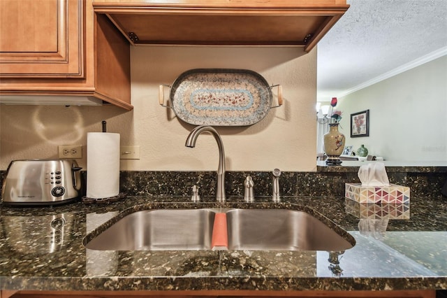 details with dark stone counters, ornamental molding, a sink, and brown cabinets