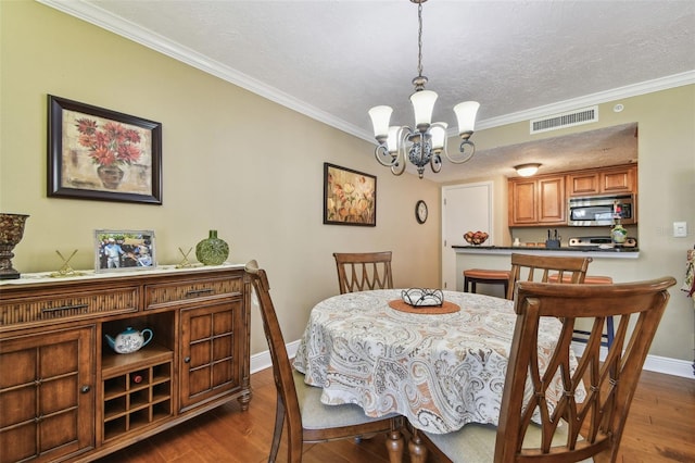 dining room with visible vents, dark wood-type flooring, crown molding, a textured ceiling, and a chandelier