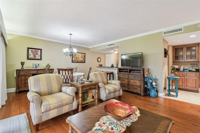 living room featuring ornamental molding, wood finished floors, visible vents, and an inviting chandelier