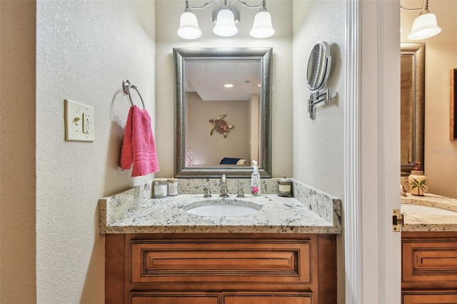 bathroom featuring a textured wall, two vanities, and a sink