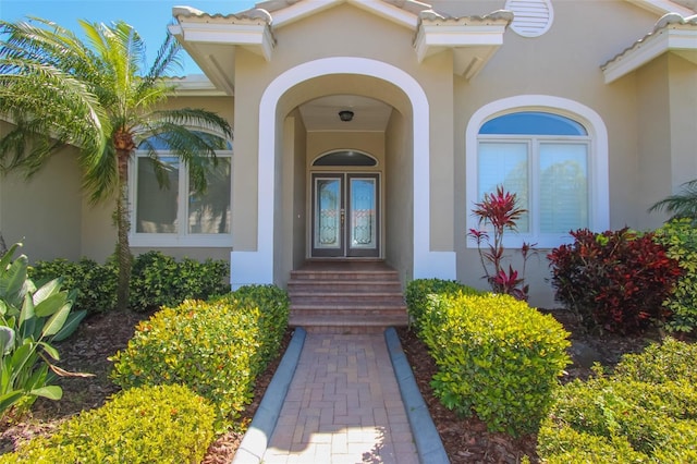 view of exterior entry with french doors, a tile roof, and stucco siding