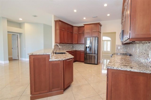 kitchen with appliances with stainless steel finishes, a peninsula, light stone countertops, a sink, and light tile patterned flooring