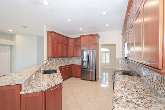 kitchen with decorative backsplash, a peninsula, light stone countertops, stainless steel appliances, and a sink