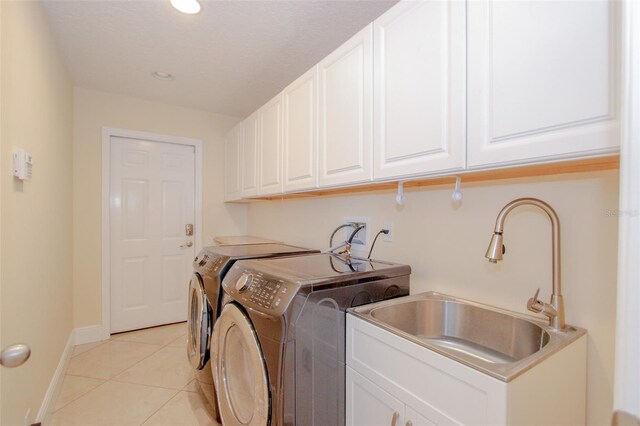 clothes washing area featuring light tile patterned flooring, a sink, baseboards, washer and dryer, and cabinet space