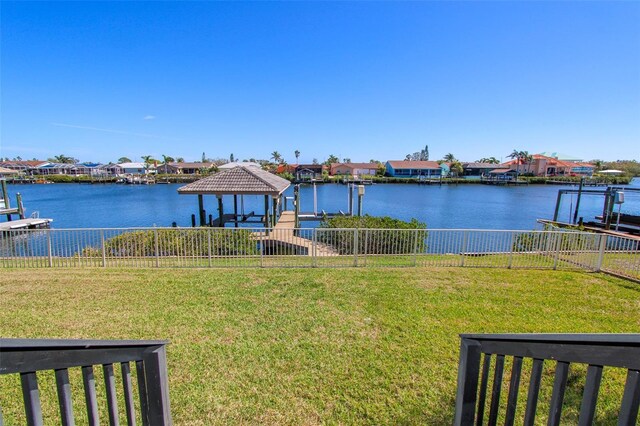 dock area with a water view, fence, and a yard