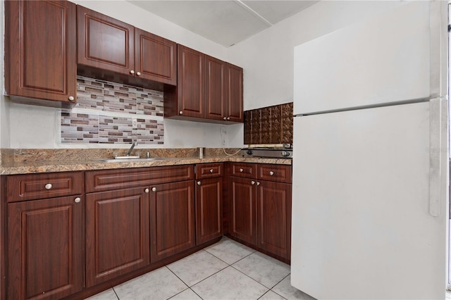 kitchen with light tile patterned floors, tasteful backsplash, freestanding refrigerator, light stone countertops, and a sink